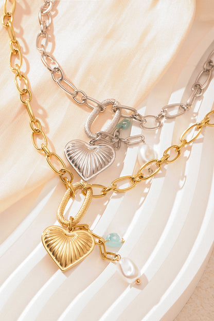 Both gold and silver heart charm chain necklaces layered together on a white textured surface
