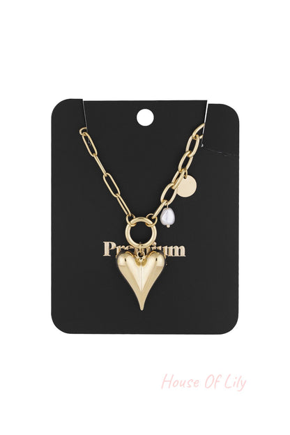 Gold-tone chunky heart pendant necklace with pearl and coin charms displayed on black packaging card