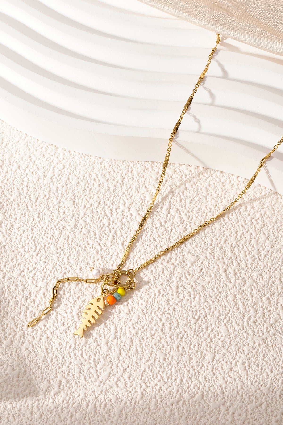 Gold fishbone pendant necklace laid on a textured white surface with bright natural lighting