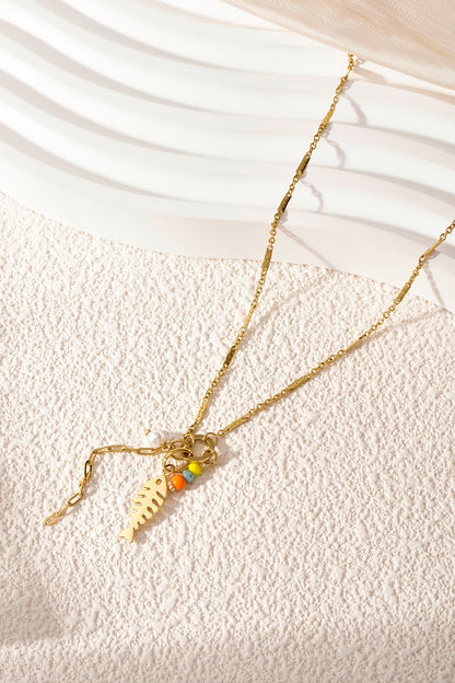 Gold fishbone pendant necklace laid on a textured white surface with bright natural lighting
