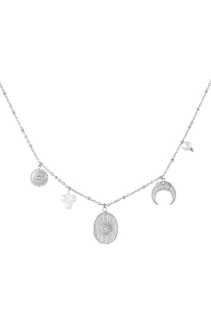 Silver-tone celestial charm pendant necklace displayed on beige curved prop highlighting texture and pearl charms