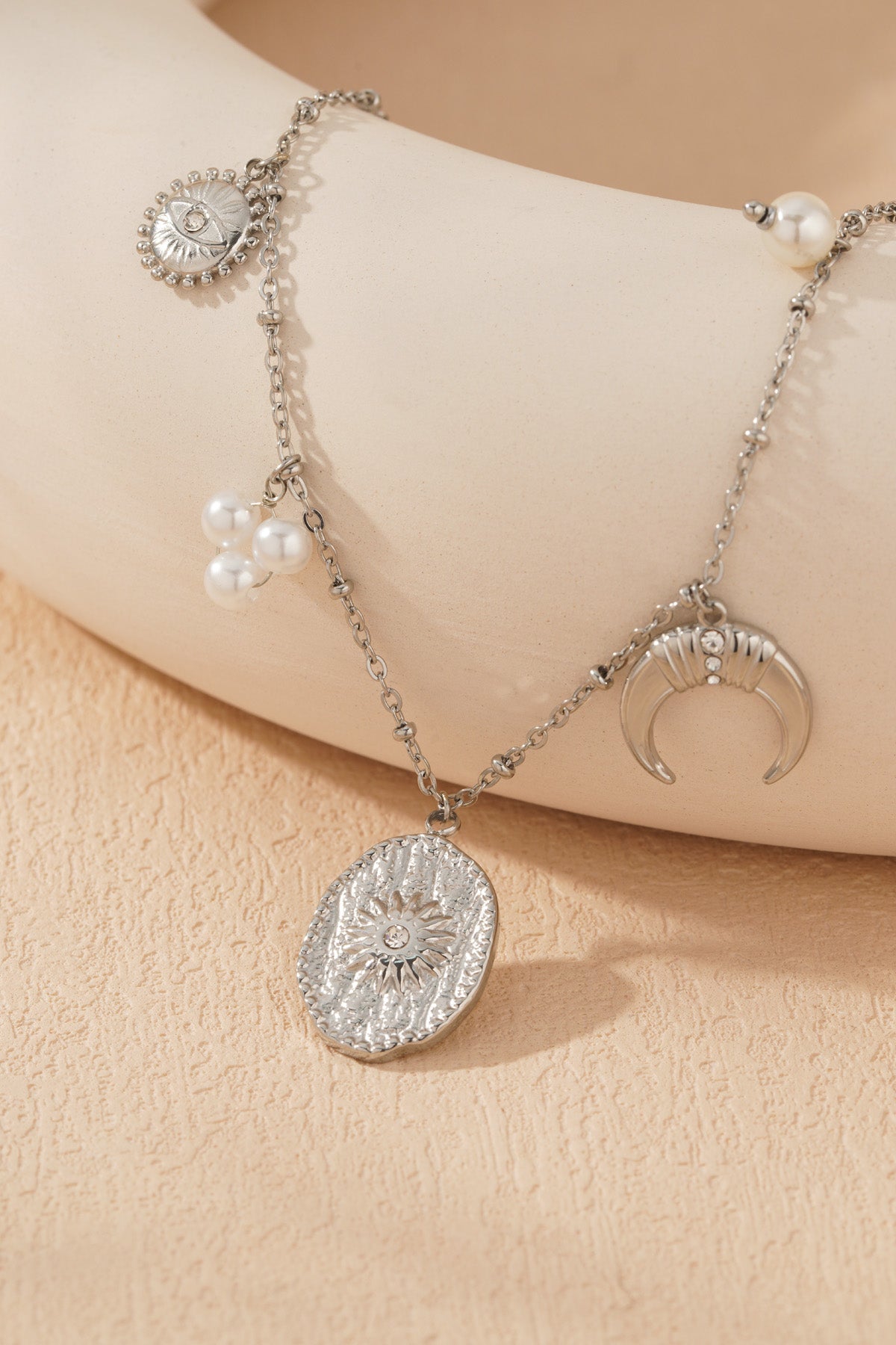 Close-up of silver-tone celestial charm necklace pendant cluster showing textured sun medallion and crescent moon with crystals