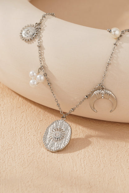 Close-up of silver-tone celestial charm necklace pendant cluster showing textured sun medallion and crescent moon with crystals