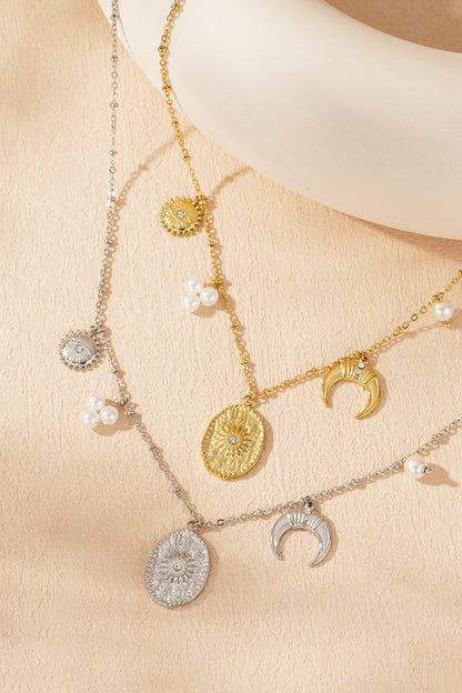 Gold and silver-tone celestial charm necklaces with sun, moon, star, and pearl accents laid flat on beige surface