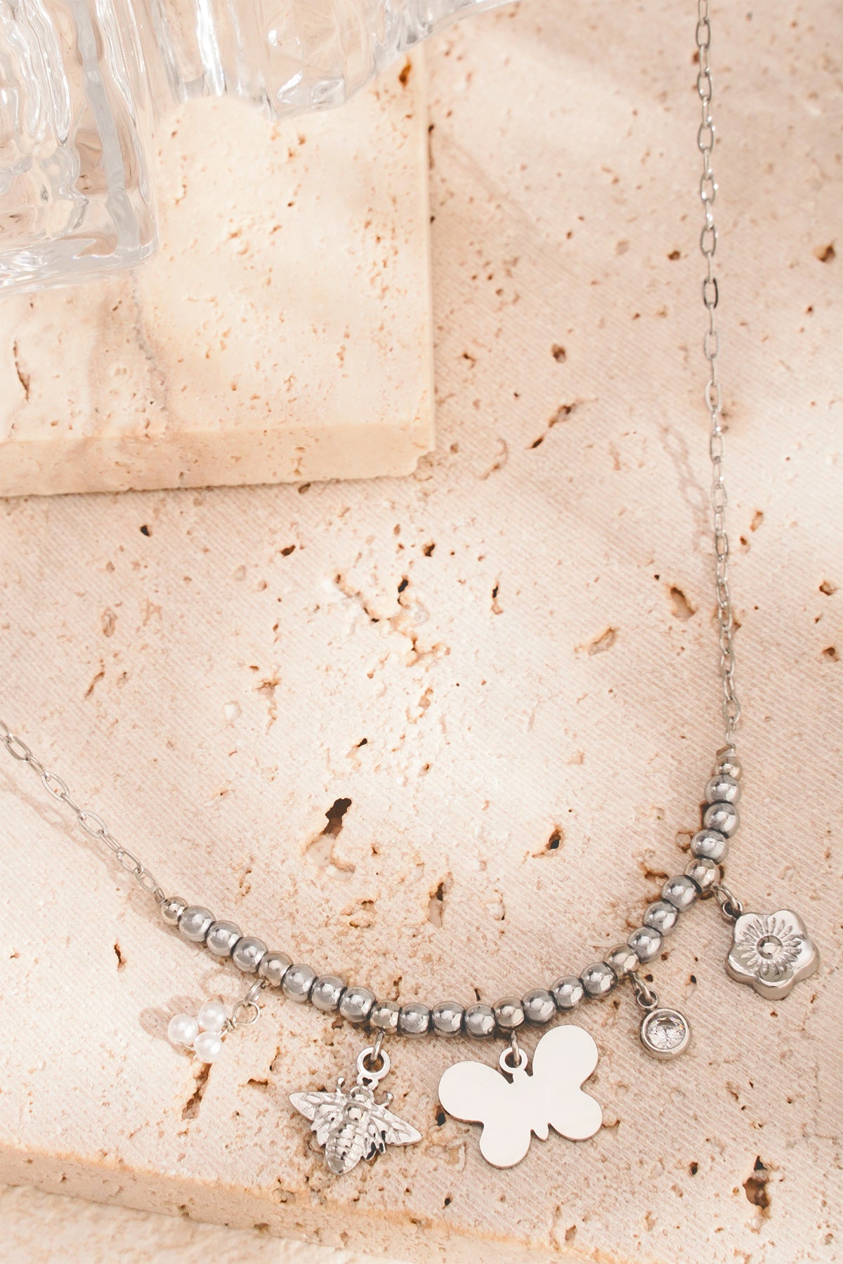 Silver charm beaded necklace with butterfly, bee and floral charms on beige background