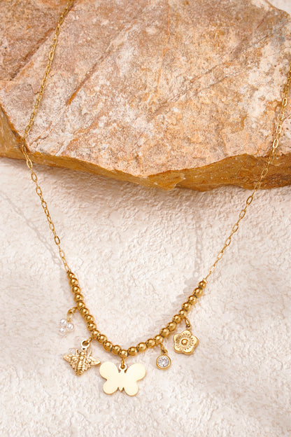 Gold charm beaded necklace with butterfly and bee charms on a rough beige stone background
