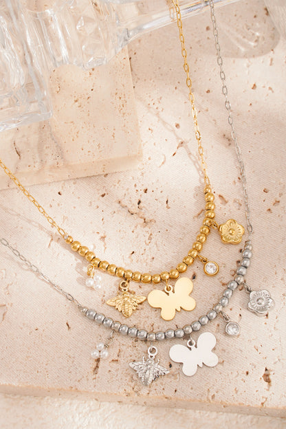 Two charm beaded necklaces in gold and silver colours on textured cream background