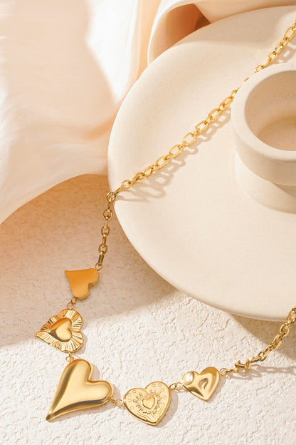 Gold multi heart charm necklace positioned on a beige ceramic dish with soft fabric background