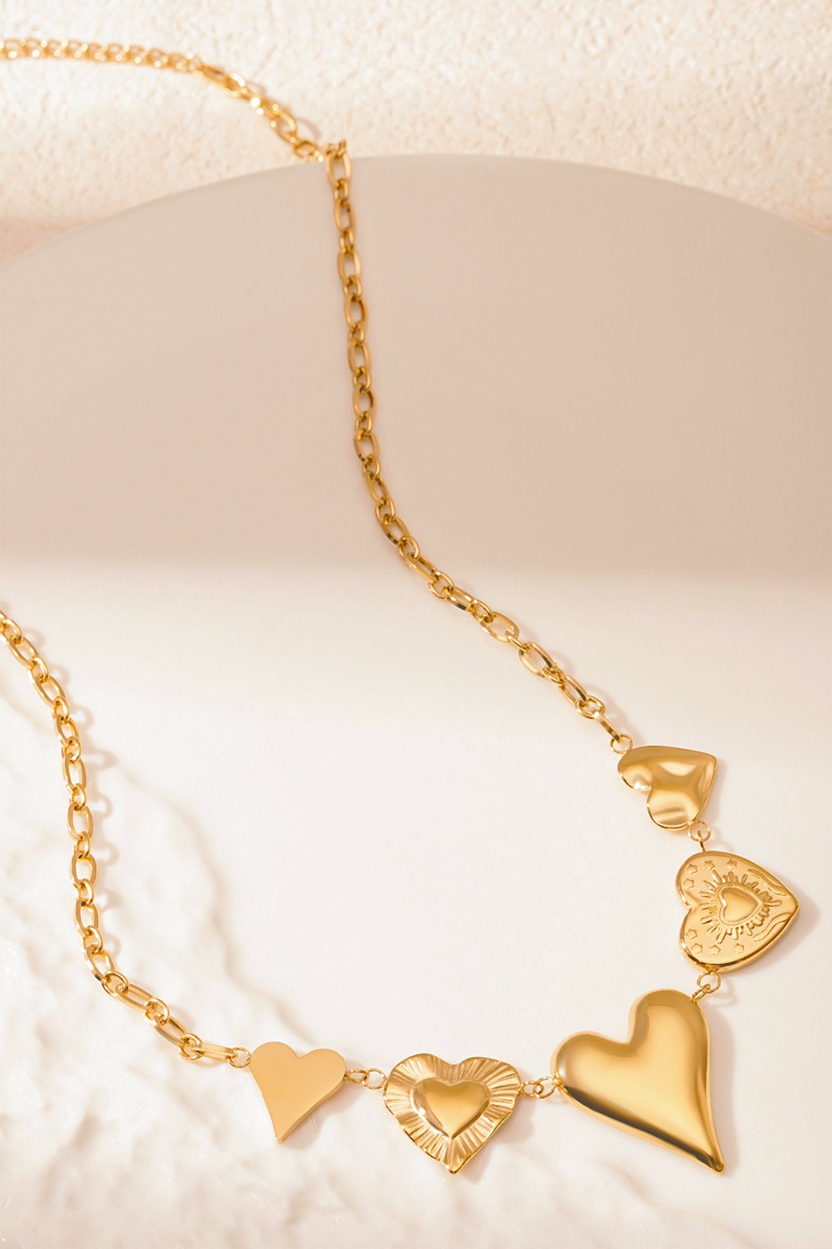 Close-up photo of gold multi heart charm necklace on a light background highlighting heart charm details