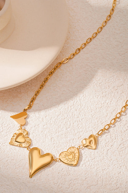 Side angled view of gold multi heart charm necklace on a cream surface showing chain and charm textures
