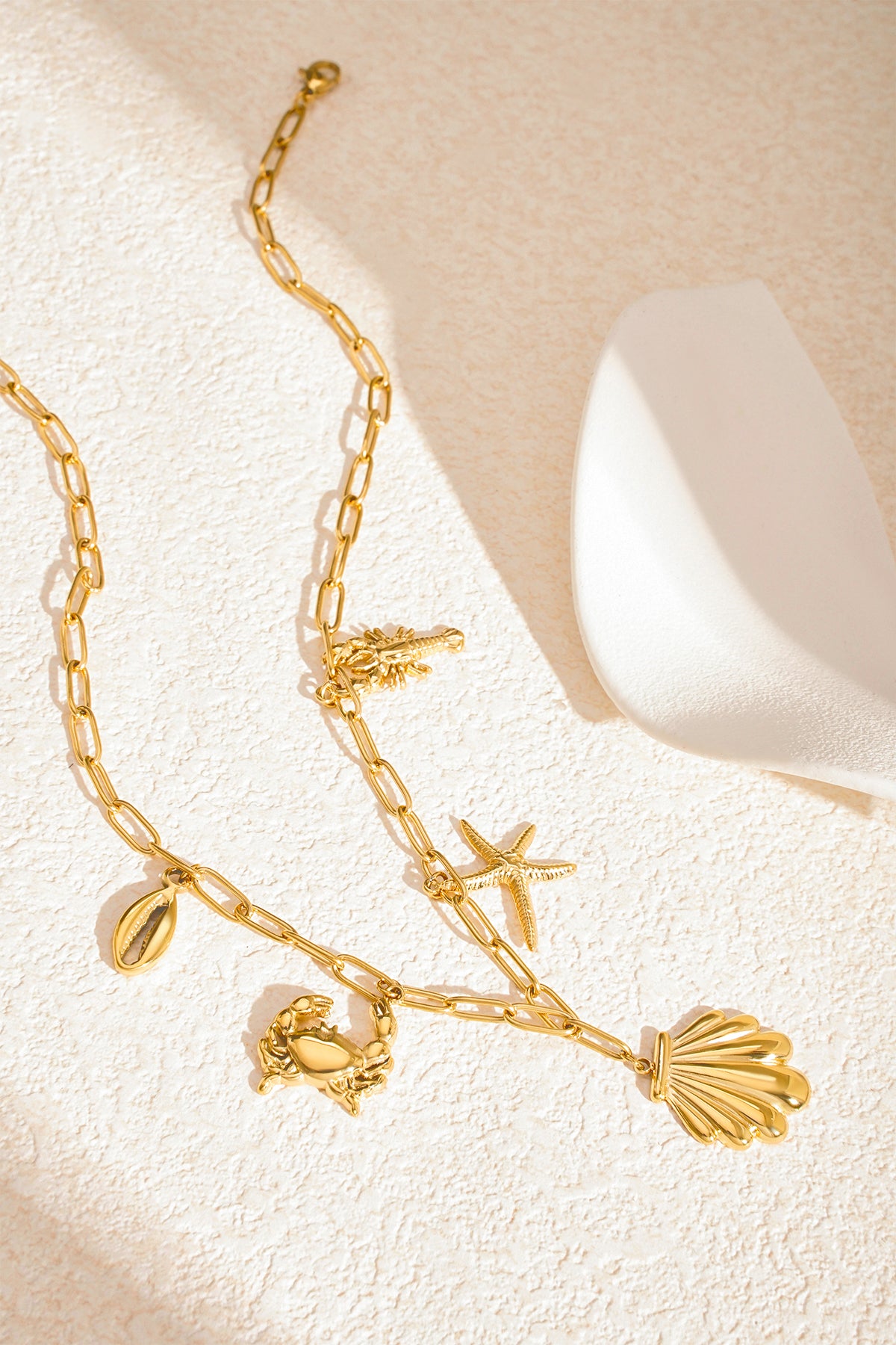Gold seaside charm necklace laid out on textured beige surface with soft shadows