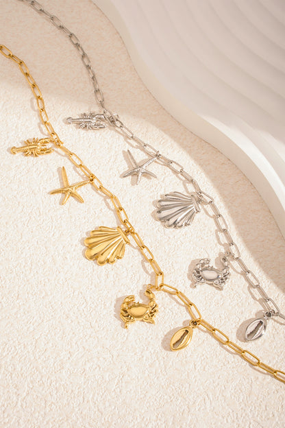 Two seaside charm necklaces in gold and silver laid on a light textured surface with sunlit highlights
