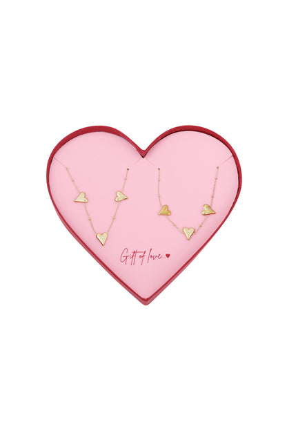 Gold-tone heart charm necklaces displayed in a pink heart-shaped gift box with red edges and the phrase 'Gift of love' inside