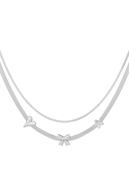 Silver layered charm necklace with heart, bow, and flower pendants on white background