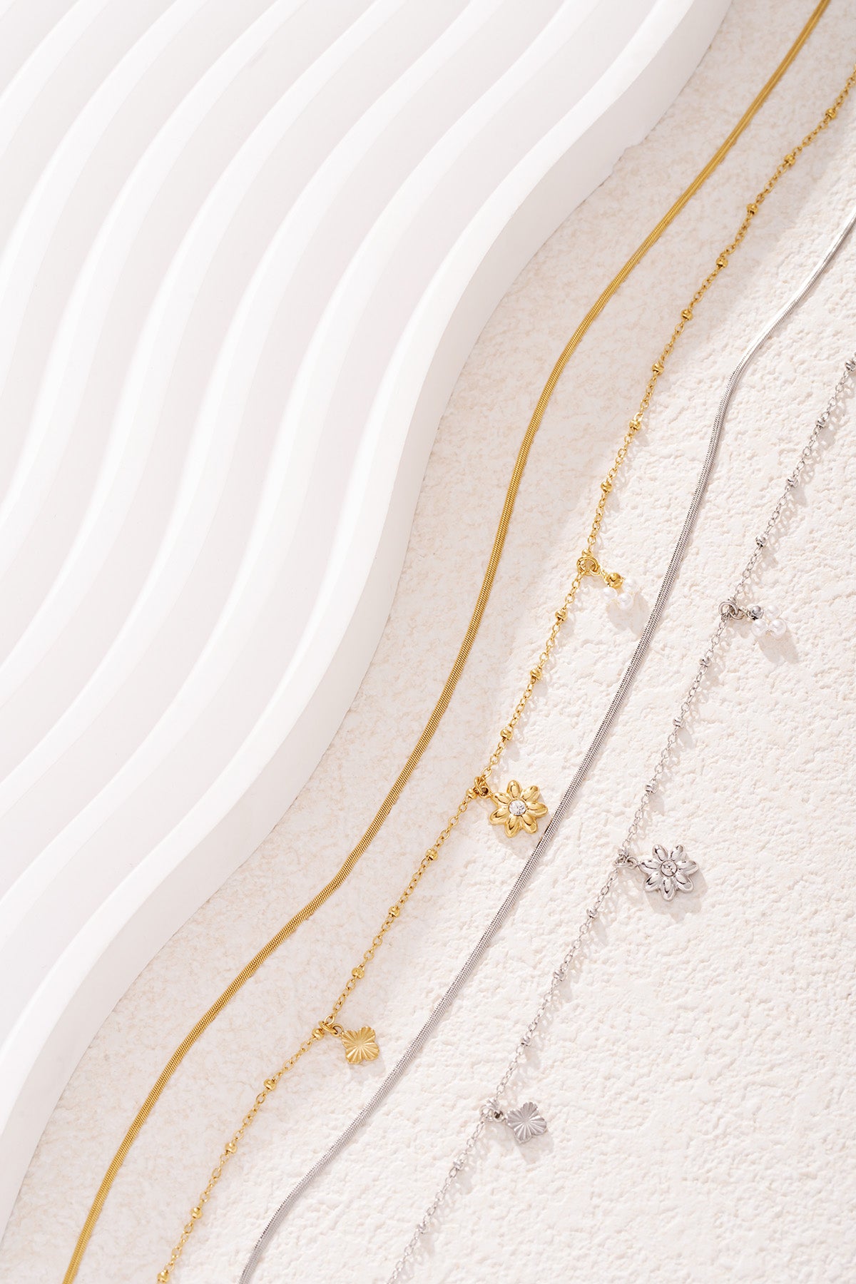 Three layered necklaces in gold and silver tones laid out on a textured white surface