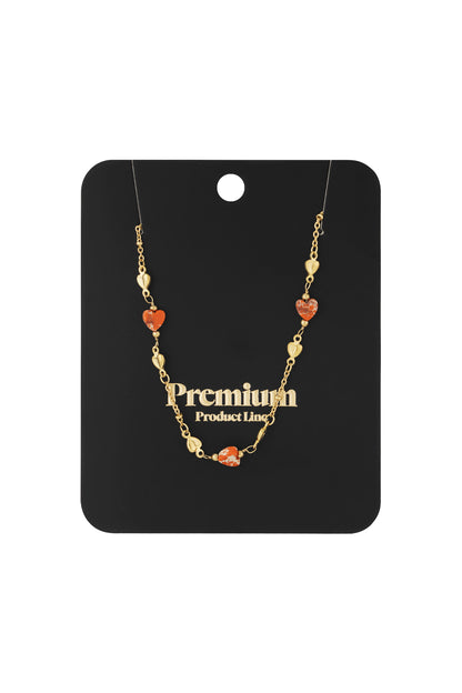 Gold-tone necklace with orange heart-shaped beads displayed on black branded card
