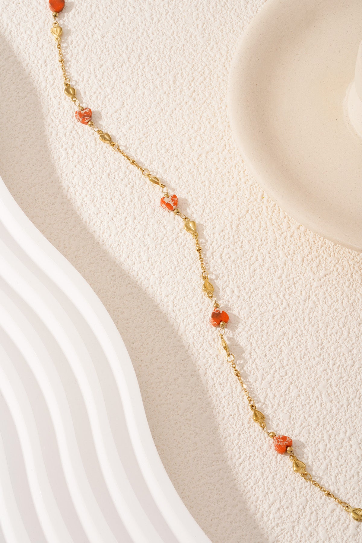 Close-up of gold-tone necklace laid out with orange heart and gold heart-shaped beads on textured white surface