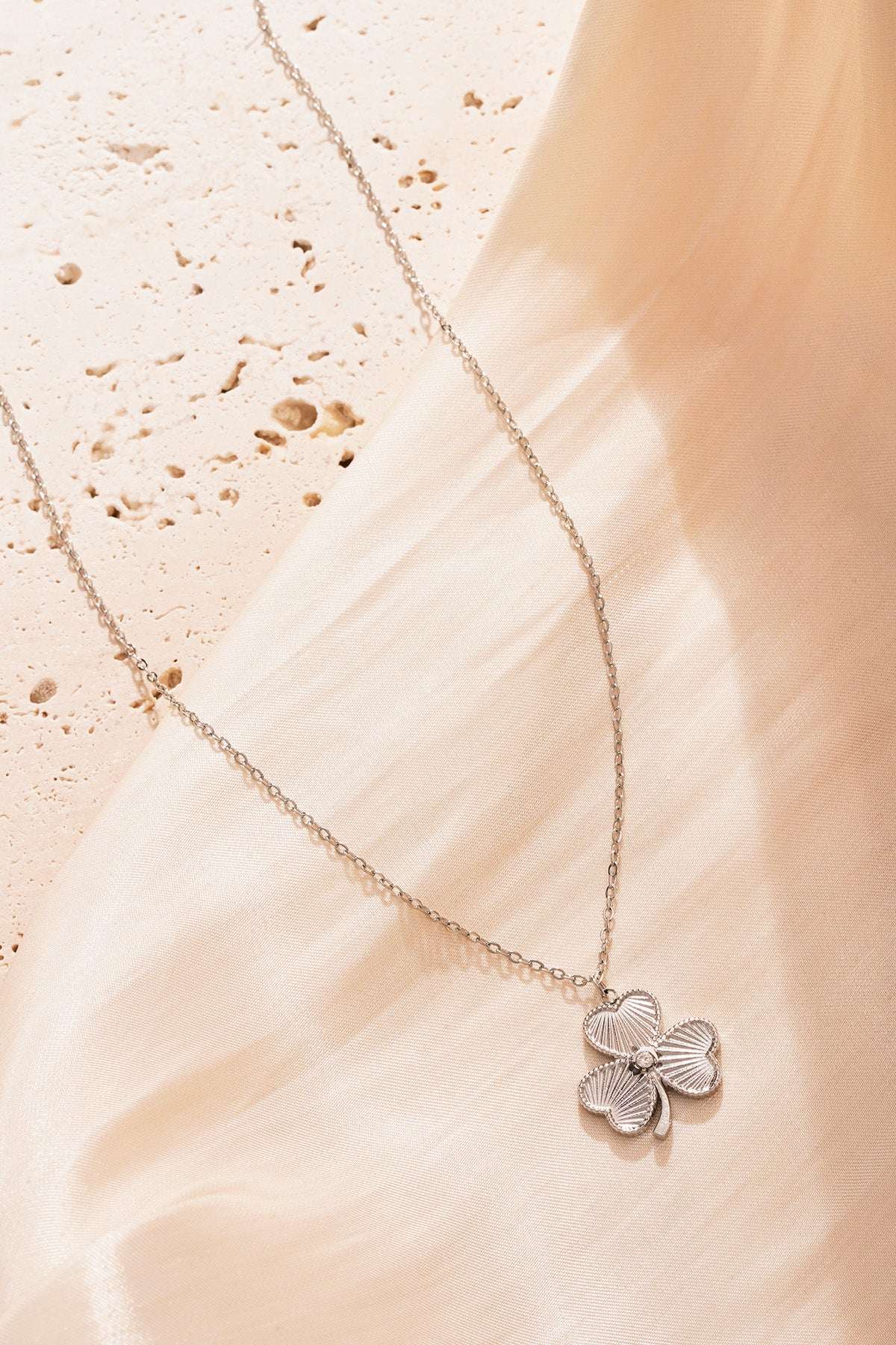 Silver clover pendant necklace showcased on soft beige fabric background giving an elegant shine