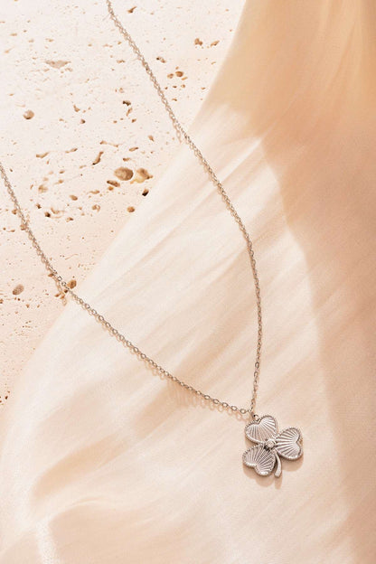 Silver clover pendant necklace showcased on soft beige fabric background giving an elegant shine