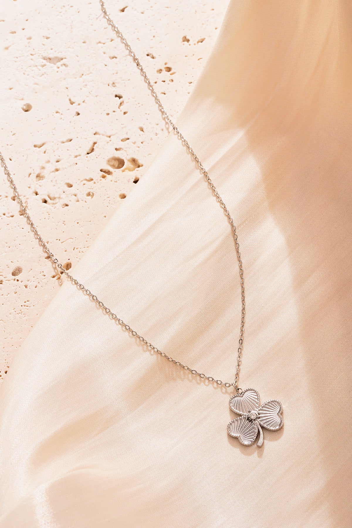 Silver clover pendant necklace showcased on soft beige fabric background giving an elegant shine