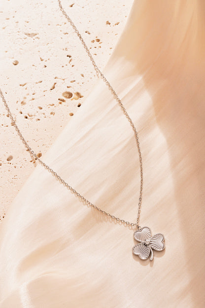 Silver clover pendant necklace showcased on soft beige fabric background giving an elegant shine