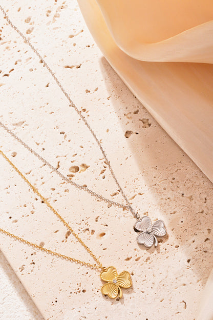 Gold and silver clover necklaces arranged on textured stone surface with a soft peach coloured fabric softly draped