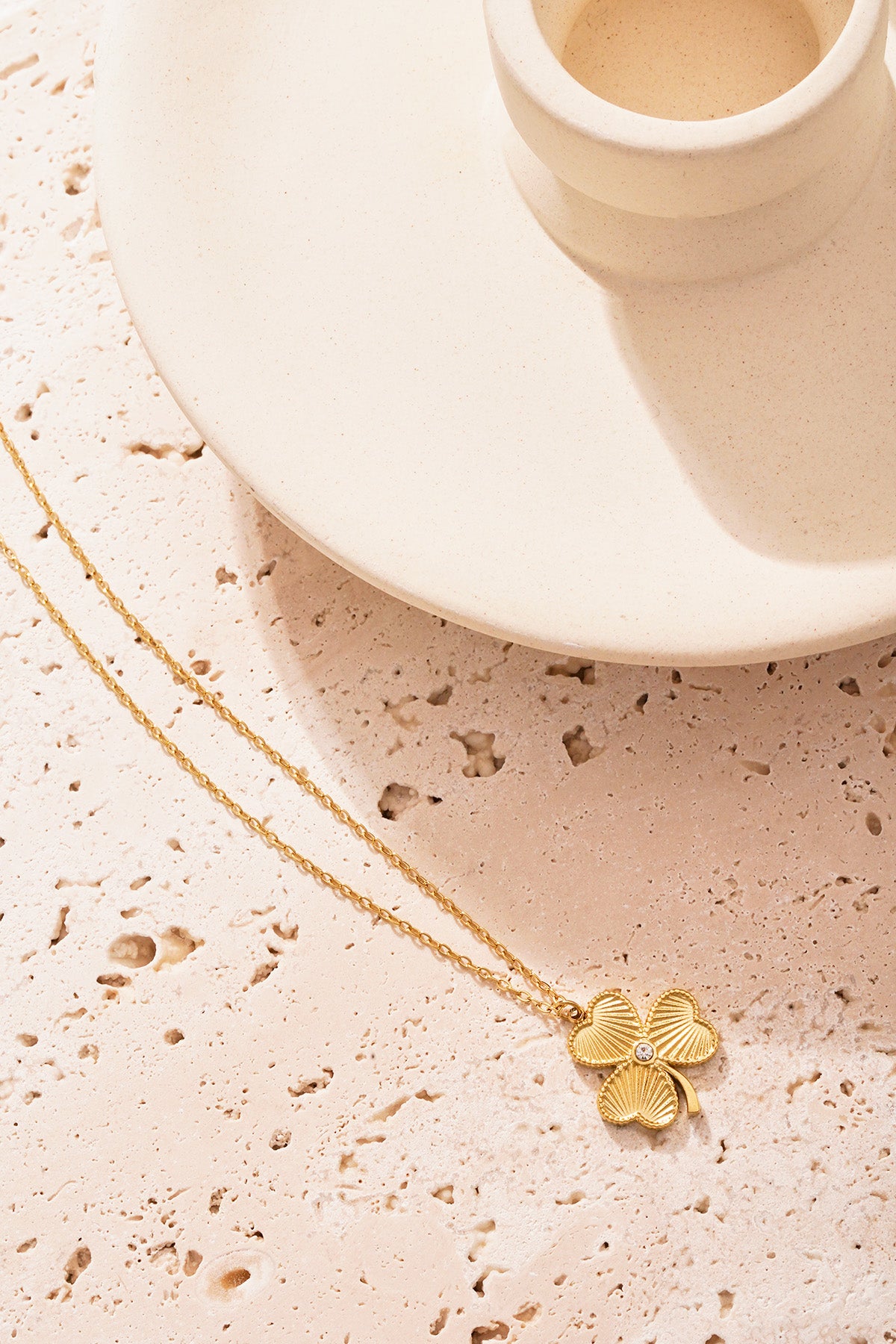 Single gold clover pendant necklace placed on a textured stone surface highlighting its intricate detail