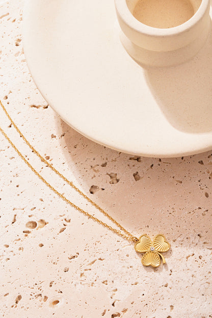 Single gold clover pendant necklace placed on a textured stone surface highlighting its intricate detail