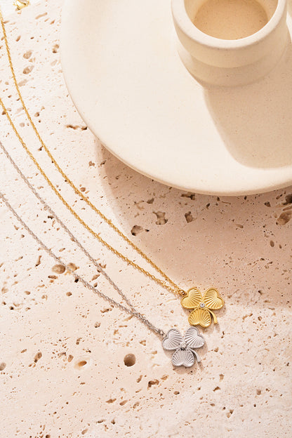 Gold and silver clover necklaces displayed on textured stone surface beside off-white ceramic holder