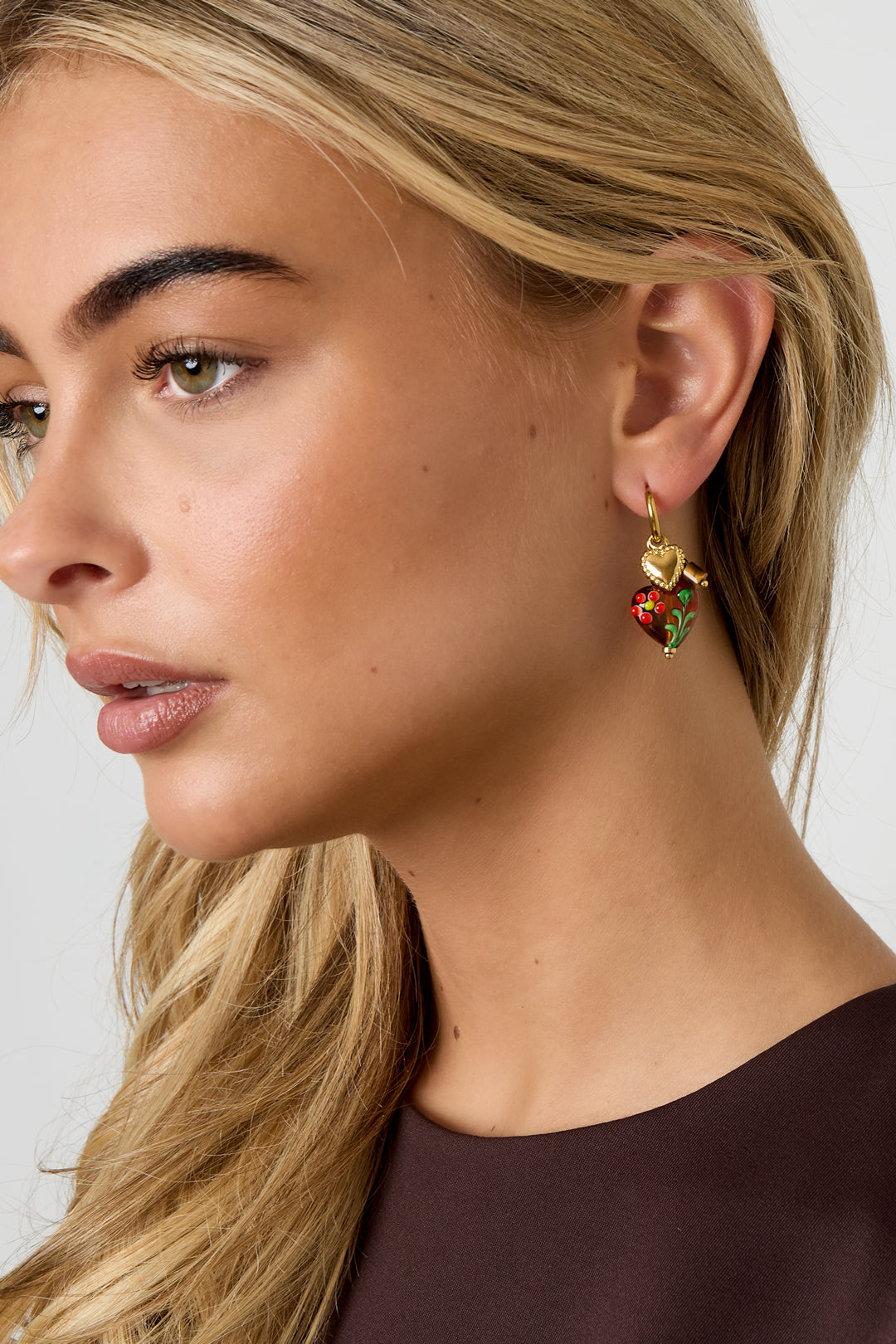 Close-up side view of woman wearing gold hoop earrings with brown floral heart charms