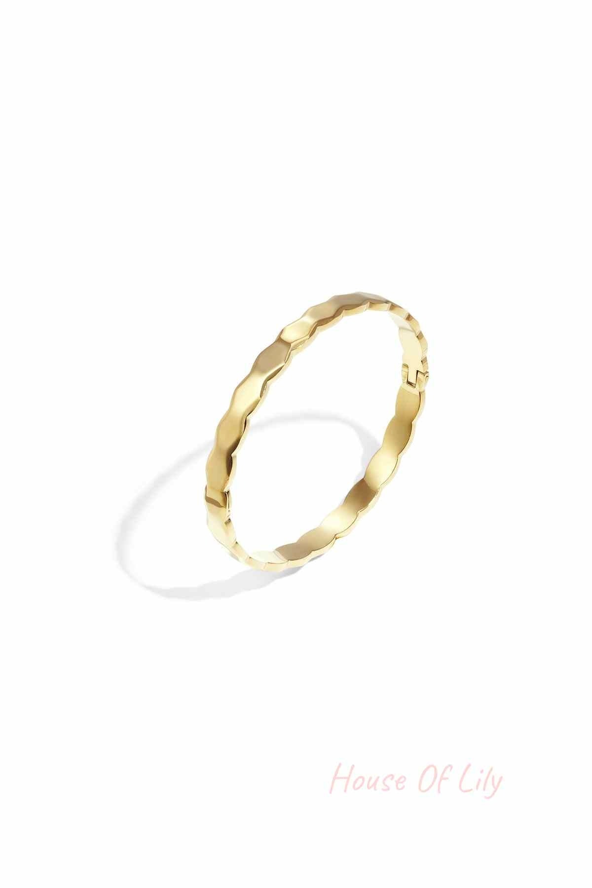Close-up of a gold scalloped edge bangle bracelet on a white background showing its wavy design and polished finish