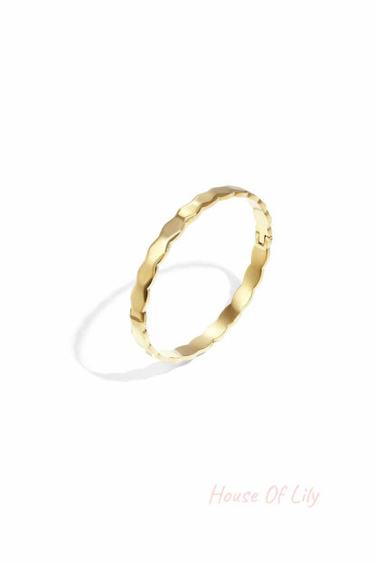 Close-up of a gold scalloped edge bangle bracelet on a white background showing its wavy design and polished finish