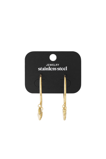 Gold stainless steel hoop earrings with dangling heart charms on a black display card.