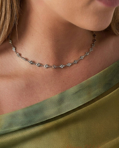 A dainty silver clover choker necklace worn around the neck.