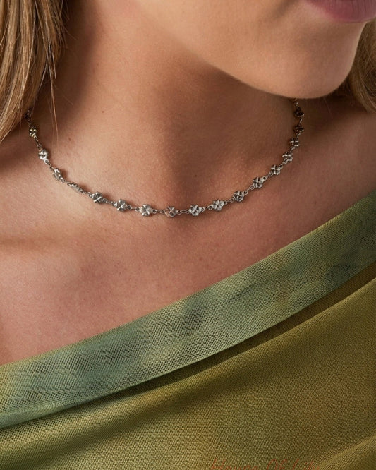 A dainty silver clover choker necklace worn around the neck.