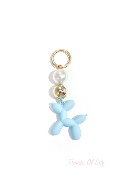 Blue balloon dog bag charm with pearl and gold beads attached to a gold ring on white background