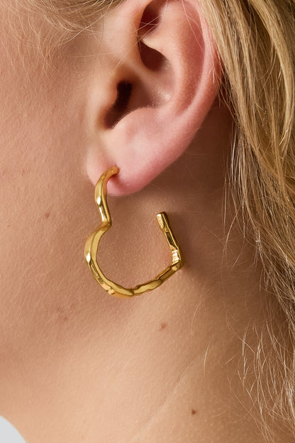 Close-up of gold wavy heart hoop earring worn on a woman's ear with blonde hair