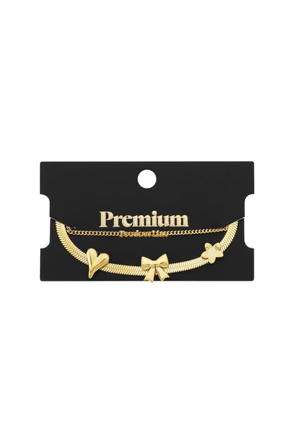 Gold-tone bangle set featuring a flat herringbone chain with heart, bow, and flower charms and a delicate link chain.