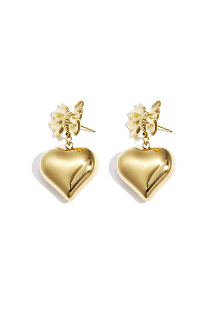 Close-up of gold dangle earrings featuring a bow knot and hanging heart charm