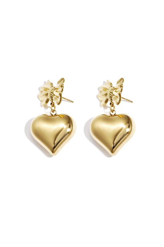 Close-up of gold dangle earrings featuring a bow knot and hanging heart charm
