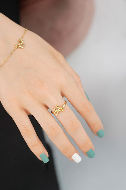 Woman's hand wearing gold bow ring with green and white nails on beige shirt