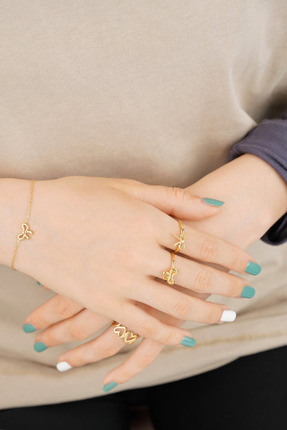 Hands showcasing multiple gold rings including bow rings and bracelet with teal and white nail polish