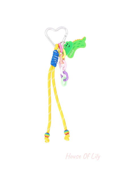 Silver heart-shaped clip bag charm with green crocodile acrylic charm, colorful pastel plastic links, yellow cord with blue accent, and rainbow beads at cord ends