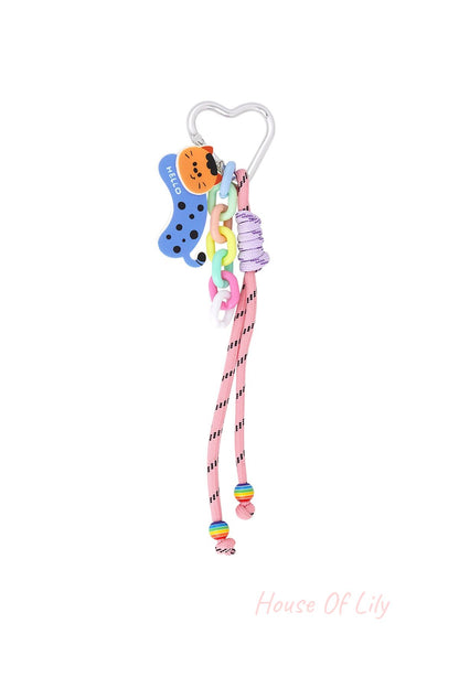Silver heart-shaped clip bag charm with orange-spotted blue cat acrylic charm, pastel plastic links, pink cord with black details, and rainbow beads