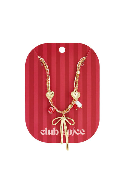 Gold chain necklace with a central bow charm, heart, pearl, and striped red beads on a red-striped backing card.