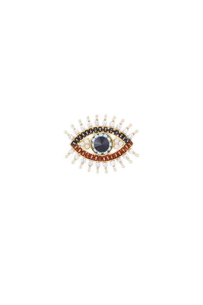 Close-up of a gold eye brooch with colorful crystal stones including black, red, white, and turquoise, arranged to mimic an eye with lashes