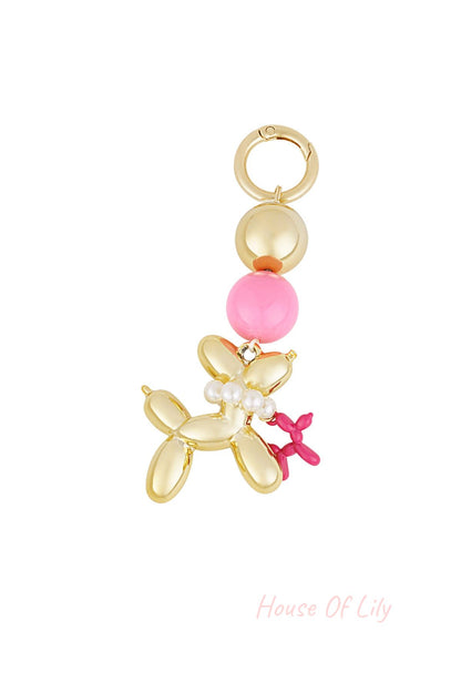 Close-up of a gold-tone balloon dog bag charm with pearl beads and pink accents against a white background