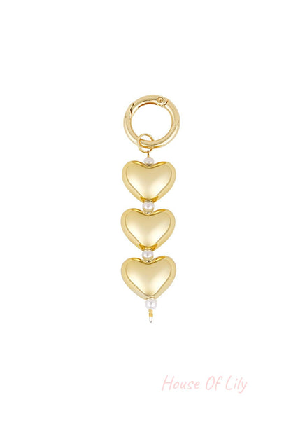 Gold bag charm featuring three heart-shaped charms separated by small white faux pearls