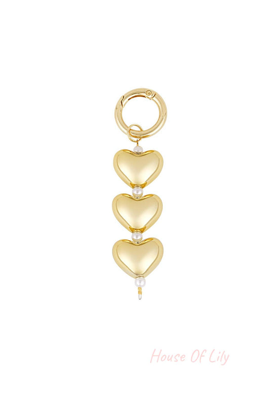Gold bag charm featuring three heart-shaped charms separated by small white faux pearls