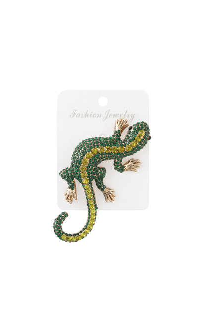 Green and yellow crystal gecko brooch displayed on a white fashion jewelry card